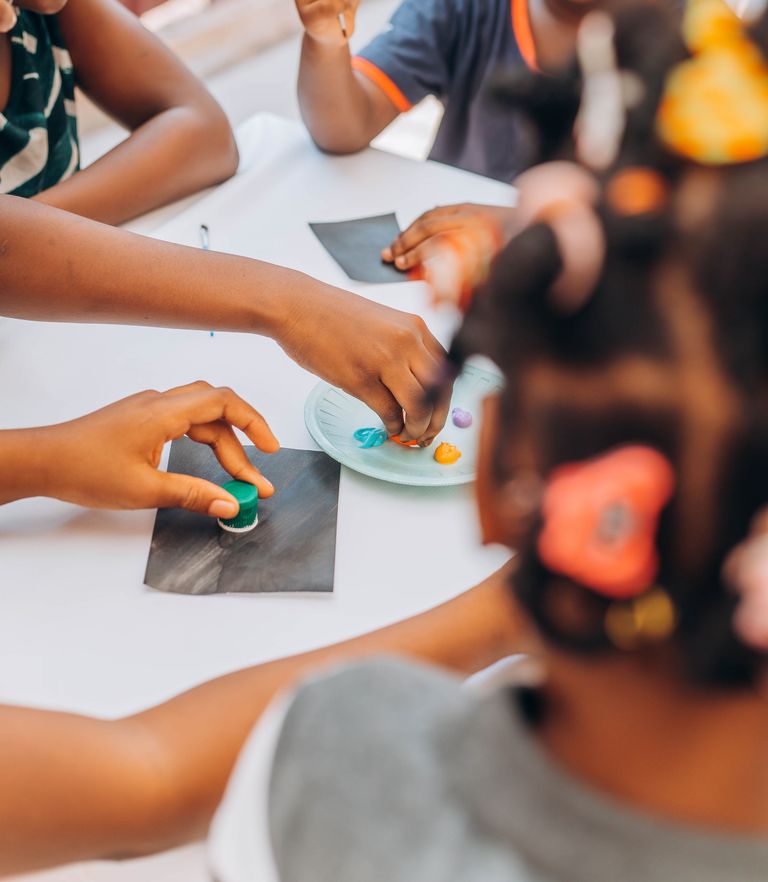 Children painting and creating art together at a table, focusing on hands and materials.
