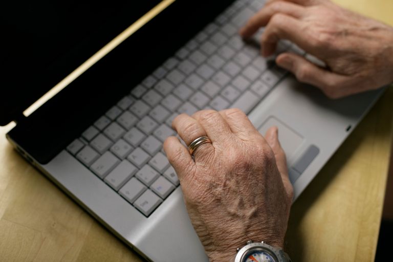 Close-up of senior hands typing on a laptop keyboard, showcasing technology use.